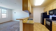 This single-floor unit offers a functional and straightforward layout designed for comfortable everyday living. The kitchen is a standout space, featuring warm wood cabinetry, granite-look countertops, and a full suite of black appliances including a refrigerator, electric range, and over-the-range microwave. A peninsula with a double sink and a breakfast bar overhang connects the kitchen to the open living area, creating an easy flow between cooking and living spaces. The kitchen is finished with durable tile flooring, while the living area transitions to wall-to-wall carpet, adding warmth underfoot. The bedroom is a well-proportioned, carpeted room filled with natural light from a pair of double-hung windows that offer views of the surrounding neighborhood. A second carpeted room with its own window provides flexibility as an additional bedroom or office space. The bathroom is clean and practical, equipped with a full soaking tub and shower combination, a single vanity with wood cabinetry and a large mirror, and safety grab bars thoughtfully installed throughout. Tile flooring and bright overhead lighting complete the bathroom's no-fuss design. Overall, the unit presents a clean, move-in-ready environment with a neutral palette throughout.