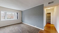This single-floor unit offers a distinctive blend of character and practicality across its well-defined living spaces. The main living area serves as the centerpiece of the home, showcasing a striking full-width painted brick accent wall in a cool gray tone that adds texture and visual interest to the room. Soft carpet underfoot and a window providing natural light complete the inviting atmosphere, while hardwood flooring transitions into adjacent areas of the unit.

The kitchen is efficiently laid out with warm wood cabinetry extending to the upper walls, dark granite-style countertops, a stainless undermount sink, and black appliances including a full-size refrigerator and range. A large window with vertical blinds floods the space with natural light, enhancing the airy feel of the room. Light wood-look tile flooring ties the kitchen together with a clean, modern finish.

The bedroom features neutral carpeting, a large window with outdoor views, a textured ceiling, and a generously sized closet door, creating a comfortable and functional retreat. An additional room displays a painted white brick wall, adding architectural consistency throughout the unit.

The bathroom is finished with full beige tile surround in the tub and shower area, accented by a decorative mosaic border tile in blue and red tones, complemented by a bright window that adds ventilation and natural light.