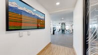 Located at 1900 S Acoma St in Denver, Colorado, this fitness center and yoga room offers a generously sized, single-floor facility designed to support a comprehensive range of workout routines. The entrance corridor welcomes visitors with warm wood-look flooring and a striking large-format artwork depicting Colorado's iconic mountain landscape, setting an energizing tone before stepping into the main exercise area.

The expansive main fitness floor features durable rubber flooring and is anchored by structural columns that define distinct workout zones. A full lineup of cardio equipment — including treadmills, ellipticals, and stationary bikes — lines the perimeter, positioned alongside large windows that flood the space with natural light and offer outdoor views. Strength training is well represented with cable machines, cable crossover towers, a full dumbbell rack with wall mirrors, adjustable benches, and free-weight stations.

A separate yoga and studio room provides a bright, open space with warm wood flooring and a distinctive orange accent ceiling. This room is equipped with stability balls and medicine balls, and benefits from multiple windows offering natural light — ideal for yoga, stretching, or group fitness sessions. Throughout both areas, the clean white walls, recessed lighting, and thoughtful layout create a modern, functional, and welcoming fitness environment.
