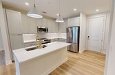 This 840-square-foot, 2-bedroom, 1-bathroom apartment at 5301 W Tyson Ave in Tampa, FL offers a modern and cohesive design throughout its single floor. The open-concept kitchen and living area serves as the heart of the unit, featuring light gray shaker cabinetry, white quartz countertops, a large central island, subway tile backsplash, and a full suite of stainless steel appliances including a refrigerator, range, microwave, and dishwasher. Stylish pendant lighting adds a contemporary touch overhead. Light wood-look flooring runs throughout the entire unit, creating a bright and seamless aesthetic. The living room is airy and well-lit, with large windows, a ceiling fan, and direct access to a private balcony overlooking lush palm trees and the surrounding community. The primary bedroom measures 180 square feet and includes a ceiling fan, natural light from a large window, and access to a closet. The second bedroom features a sliding barn door and the same warm wood flooring. The bathroom is clean and modern, finished with white tile, a glass-enclosed walk-in shower, and a white quartz vanity. A private balcony with black metal railings completes this well-appointed Tampa apartment.