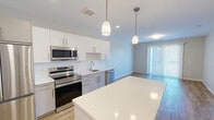 Located at 83 Pleasant Valley St in Methuen, Massachusetts, this one-bedroom, one-bathroom unit offers a thoughtfully designed layout with modern finishes throughout. The open-concept kitchen and dining area serves as the heart of the home, featuring a large center island with pendant lighting, crisp white cabinetry, a classic subway tile backsplash, and a full suite of stainless steel appliances including a French door refrigerator, electric range, and over-the-range microwave. Light hardwood-style flooring runs through the main living areas, enhancing the bright, airy atmosphere. The living and dining space benefits from a floor-to-ceiling sliding glass door dressed with vertical blinds, allowing generous natural light to fill the room. The bedroom is a comfortable, carpeted retreat with a large window overlooking the surrounding area, providing ample natural light. A dedicated closet offers convenient storage. The bathroom features a sleek vanity with a white countertop, an undermount sink, and a large mirror with overhead lighting, maintaining the clean, contemporary aesthetic found throughout the unit. Neutral tones and clean lines define the overall ambiance, creating a move-in-ready space well suited for modern living.
