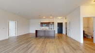 Located at 11130 N Buntrock Ave in Mequon, Wisconsin, this single-floor residence offers a thoughtfully designed open-concept layout with clean, contemporary finishes throughout. The expansive main living area is anchored by warm-toned hardwood-style flooring that flows seamlessly from the living space into the kitchen, creating a cohesive and airy feel. Large windows and a sliding glass door lead to a private balcony, filling the space with natural light and providing outdoor access.

The kitchen is a standout feature, centered around a substantial island with a built-in sink and pendant lighting overhead. Rich dark-wood cabinetry contrasts beautifully with light countertops, while stainless steel appliances — including a refrigerator, range, and over-the-range microwave — complete the space with a modern, functional aesthetic.

The bedroom features plush neutral carpeting and offers convenient access to both a closet and the main living area. Two bathrooms serve the unit: one with a tiled tub-shower combination and a dark-wood vanity, and a second with a walk-in glass-enclosed shower, a spacious vanity with ample drawer storage, and a large mirror. Both bathrooms feature subway tile and light stone-look tile flooring, maintaining a consistent and refined design language throughout the home.