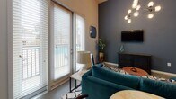 Located at 725 Coleman Blvd in Mount Pleasant, South Carolina, this single-floor studio unit offers a thoughtfully designed open-concept layout that seamlessly integrates the living, sleeping, and kitchen areas into one cohesive space. The living area features soaring ceilings, a striking multi-bulb chandelier, and a bold accent wall in a deep slate blue, creating a modern and inviting atmosphere. Large French doors flood the space with natural light and provide direct access to an outdoor patio, offering pleasant views of the surrounding area. The kitchen is outfitted with dark espresso cabinetry, granite countertops, stainless steel appliances including a range, microwave, and refrigerator, and a double-basin sink with a contemporary pull-down faucet. A dining area adjacent to the kitchen benefits from additional natural light via a second set of French doors. The bathroom is well-appointed with a granite-topped vanity, dark wood cabinetry, a full tub-shower combination with white tile surround, and a curved shower rod. Throughout the unit, the consistent use of neutral tones, granite surfaces, and modern fixtures contributes to a clean, contemporary aesthetic well-suited to the Mount Pleasant lifestyle.