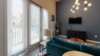 Located at 725 Coleman Blvd in Mount Pleasant, South Carolina, this single-floor studio unit offers a thoughtfully designed open-concept layout that seamlessly integrates the living, sleeping, and kitchen areas into one cohesive space. The living area features soaring ceilings, a striking multi-bulb chandelier, and a bold accent wall in a deep slate blue, creating a modern and inviting atmosphere. Large French doors flood the space with natural light and provide direct access to an outdoor patio, offering pleasant views of the surrounding area. The kitchen is outfitted with dark espresso cabinetry, granite countertops, stainless steel appliances including a range, microwave, and refrigerator, and a double-basin sink with a contemporary pull-down faucet. A dining area adjacent to the kitchen benefits from additional natural light via a second set of French doors. The bathroom is well-appointed with a granite-topped vanity, dark wood cabinetry, a full tub-shower combination with white tile surround, and a curved shower rod. Throughout the unit, the consistent use of neutral tones, granite surfaces, and modern fixtures contributes to a clean, contemporary aesthetic well-suited to the Mount Pleasant lifestyle.