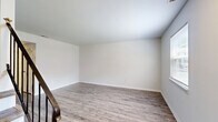 This two-bedroom, two-bathroom two-story home in Hampton, Virginia offers a clean, modern aesthetic throughout. The main floor houses an open-concept dining area and kitchen, a living room, a full bathroom, and a dedicated laundry space. The kitchen stands out with crisp white shaker-style cabinetry, granite-look countertops, stainless steel appliances including a range, microwave, dishwasher, and refrigerator, plus a double sink beneath a window overlooking greenery. Crown molding and a track light fixture add a refined touch. The living room is bright and welcoming, featuring wood-look laminate flooring and a staircase with a sleek black metal railing leading to the upper level. Upstairs, two well-sized bedrooms offer neutral tones, wood-look flooring, and ample closet space — with five closets distributed throughout the home. The second floor also hosts a full bathroom with beadboard wainscoting, a vanity with medicine cabinet, and a tub-shower combo. Both levels maintain a cohesive, light-filled palette of white walls and warm-toned flooring, giving the home a fresh and move-in-ready feel.