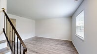 This two-bedroom, two-bathroom two-story home in Hampton, Virginia offers a clean, modern aesthetic throughout. The main floor houses an open-concept dining area and kitchen, a living room, a full bathroom, and a dedicated laundry space. The kitchen stands out with crisp white shaker-style cabinetry, granite-look countertops, stainless steel appliances including a range, microwave, dishwasher, and refrigerator, plus a double sink beneath a window overlooking greenery. Crown molding and a track light fixture add a refined touch. The living room is bright and welcoming, featuring wood-look laminate flooring and a staircase with a sleek black metal railing leading to the upper level. Upstairs, two well-sized bedrooms offer neutral tones, wood-look flooring, and ample closet space — with five closets distributed throughout the home. The second floor also hosts a full bathroom with beadboard wainscoting, a vanity with medicine cabinet, and a tub-shower combo. Both levels maintain a cohesive, light-filled palette of white walls and warm-toned flooring, giving the home a fresh and move-in-ready feel.