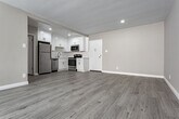 Located in the vibrant Los Feliz neighborhood of Los Angeles, this single-floor unit at 1840 Winona Blvd offers a clean, modern aesthetic throughout. The open-concept living area is anchored by light gray wood-style flooring that flows seamlessly throughout the space, complementing the neutral warm-gray walls and crisp white trim. Large sliding glass doors dressed with vertical blinds bathe the living room in natural light and provide direct access to a balcony, enhancing the sense of openness. A wall-mounted air conditioning unit adds convenient climate control to the main living area.

The kitchen is thoughtfully designed with bright white shaker-style cabinetry extending to the ceiling for ample storage, paired with light quartz countertops and a full suite of stainless steel appliances, including a refrigerator, electric range, microwave, and dishwasher. Recessed lighting illuminates the kitchen and adjacent dining area, creating a welcoming atmosphere.

The bedroom features a spacious closet with built-in shelving and organizational systems, offering generous storage. The bathroom is finished with clean white subway tile surrounding the soaking tub and shower combination, brushed nickel fixtures, and a crisp, minimalist design. Throughout, the unit presents a well-maintained, move-in-ready condition with a cohesive and contemporary feel.