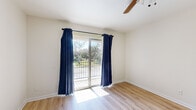 This single-story 2-bedroom, 1-bathroom home offers a thoughtfully laid-out floor plan that maximizes its compact footprint. Light wood-style flooring runs consistently throughout all rooms, lending a clean, cohesive aesthetic to the entire space.

The open living room is bright and airy, featuring a ceiling fan and sliding glass doors framed by bold navy curtains that lead to an outdoor balcony with views of surrounding greenery. A pass-through counter connects the living area to the kitchen, which is well-appointed with white shaker-style cabinetry, granite-look countertops, a double stainless steel sink, pendant lighting, and a warm mosaic tile backsplash in earthy tones.

The primary bedroom is generously sized, offering a ceiling fan, sliding balcony access, and abundant natural light through large glass doors. The second bedroom features a wide window with blinds, flooding the room with natural light. Both bedrooms include closet storage, with the primary bedroom featuring a dedicated walk-in closet with built-in shelving.

The bathroom is clean and functional, featuring a tub-shower combination, white vanity with stone-look countertop, overhead lighting, a large mirror, and additional overhead cabinetry for storage. A hallway connects all rooms efficiently, completing this well-organized and move-in ready home.