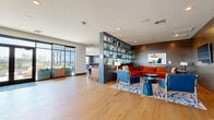 Located at 601 Press Place in Nashville's vibrant Germantown neighborhood, this upscale amenity space at The Hamilton offers a thoughtfully designed blend of indoor and outdoor living. The generously sized interior is finished with wide-plank hardwood flooring throughout and is organized into several distinct zones. A sleek bar area anchors one section of the lounge, highlighted by a striking blue herringbone tile backsplash, pendant lighting with gold accents, and bar seating along a dark wood counter. Adjacent lounge areas feature plush seating arrangements, including a bold rust-orange sectional sofa set against a dark shiplap accent wall with a wall-mounted TV and built-in shelving displaying curated décor. A patterned geometric tile floor defines a separate seating nook furnished with round accent chairs and a contemporary coffee table. The game room area provides an entertainment focal point with a full-size billiards table and a oversized Connect Four game. Floor-to-ceiling windows and glass doors flood the interior with natural light and frame views of the Nashville skyline. The entrance features a mosaic tile accent wall and Hamilton-branded entry mat. Outdoors, a spacious rooftop terrace offers panoramic skyline views, woven lounge chairs, lush planters, and a bar-height dining table — ideal for relaxing or entertaining al fresco.