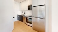 Located on the second floor at 3920 W 5th St in Los Angeles' Koreatown neighborhood, this modern studio unit offers a thoughtfully designed open-concept layout that maximizes every square foot. The living and sleeping areas flow seamlessly together, featuring light hardwood flooring, crisp white walls, and recessed lighting that contribute to a clean, airy ambiance. A large window allows natural light to fill the space, creating a bright and welcoming atmosphere throughout the day.

The sleeping area includes a built-in workstation with white cabinetry and overhead storage, as well as a wall-mounted TV — making the space both functional and efficient. A compact sitting area with modular seating and a round coffee table defines the living zone, completing the open floor plan.

The kitchen is well-appointed with stainless steel appliances, including a full-size refrigerator, electric range, built-in microwave, and dishwasher. Two-tone cabinetry — white uppers paired with dark lower cabinets — frames a classic white subway tile backsplash, lending a contemporary yet timeless aesthetic.

The bathroom features large-format light gray tile flooring and a walk-in shower with floor-to-ceiling tile surround and a glass enclosure, finished with matte black fixtures and hardware for a modern, cohesive look.