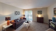 This single-story residence offers a well-organized layout across several distinct living spaces. The kitchen is outfitted with white shaker-style cabinetry, dark granite-look countertops, a double stainless steel sink, a dishwasher, and a striking mosaic tile backsplash in neutral earth tones. Wood-style flooring runs through the kitchen and flows into the adjacent dining and entry areas, adding warmth and visual continuity.

The entry area transitions seamlessly into a carpeted living room, which serves as the central gathering space. A large sliding glass door floods the room with natural light and provides direct access to an outdoor patio with views of surrounding greenery. The dining area sits nearby, illuminated by a pendant light fixture.

The bedrooms are carpeted and feature neutral walls, with the primary bedroom benefiting from multiple windows that allow ample natural light. An additional room with carpet and a window offers flexible use as a bedroom or den.

Two bathrooms mirror each other in design, each featuring white vanity cabinetry, dark countertops, wood-style flooring, and well-lit vanity mirrors. The overall ambiance throughout the residence is bright, clean, and cohesive, with a consistent neutral color palette that lends a calm, livable atmosphere.