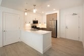 Located at 18831 Von Karman Ave in Irvine, CA, this well-appointed three-bedroom, two-bathroom unit offers a thoughtfully designed single-floor layout with a bright, modern aesthetic throughout. The open-concept kitchen and living area serves as the heart of the home, featuring a central island with a white quartz countertop, dual-basin stainless steel sink, and pendant lighting overhead. The kitchen is equipped with a full suite of stainless steel appliances — including a gas range, over-the-range microwave, dishwasher, and refrigerator — complemented by a two-tone cabinetry design pairing crisp white upper cabinets with warm wood-tone lower cabinets. Light wood-grain flooring flows throughout the main living areas, adding warmth and continuity to the space. The three bedrooms offer a comfortable sense of scale, with the generously sized primary bedroom featuring plush carpeting, a ceiling fan, and access to a dedicated closet with dual hanging rods. Additional bedrooms are finished with light flooring and natural light from well-placed windows. The bathrooms feature clean white countertops, wood-tone vanity cabinetry, and modern fixtures. A walk-in closet with wrap-around shelving provides ample storage. The overall ambiance is clean, contemporary, and move-in ready.
