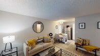 This single-floor residence offers a thoughtfully designed layout that maximizes comfort and functionality throughout. The open-concept living area serves as the heart of the home, featuring light wood-style flooring, neutral gray walls, and a textured ceiling that adds subtle character. Natural light flows in through windows dressed with white curtains and blinds, brightening the space. A round wall mirror and carefully chosen accents create a modern, cohesive aesthetic.

The living area flows seamlessly into the dining space, which sits adjacent to the kitchen — ideal for everyday convenience. The kitchen is well-equipped with white cabinetry, light countertops, a stainless steel refrigerator, a gas range, and a single-basin sink, all set against light flooring and flush ceiling lighting.

The bedroom is a serene retreat, featuring the same light flooring, ample natural light from a well-positioned window, and a textured ceiling. A round mirror and dresser add practical elegance to the room.

The bathroom is clean and efficiently designed, with a white vanity, a large framed mirror, and bright overhead lighting, offering a fresh and functional space. Throughout, the residence maintains a consistent, modern aesthetic with neutral tones and quality finishes.
