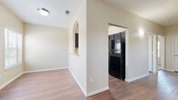 This single-floor residence offers a thoughtfully arranged layout with a cohesive blend of practical design and comfortable living spaces. The main living area greets you with rich wood-look flooring, warm neutral walls, and a ceiling fan that adds both style and function. A large window with horizontal blinds fills the space with natural light, creating an inviting atmosphere near the front entry door.

The kitchen is equipped with dark espresso cabinetry, light-toned countertops, and black appliances including a gas range and a full-size refrigerator. Wood-look flooring continues throughout, and a distinctive arched pass-through window connects the kitchen corridor to the living area, adding an architectural detail that enhances the open feel of the home.

The bedrooms feature plush wall-to-wall carpeting and windows dressed with horizontal blinds, allowing for natural light and views of the surrounding area. Each bedroom includes closet access, providing practical storage. The bathroom is finished with wood-look tile flooring, a full tub and shower combo with clean white tile surround, and chrome hardware accents.

Throughout the residence, consistent warm beige tones, white trim, and clean lines tie each room together, creating a unified and comfortable living environment.