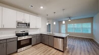Located at 5697 SW 49th Rd in Ocala, Florida, this well-appointed single-story home offers three bedrooms and two bathrooms thoughtfully arranged across a comfortable floor plan. The open-concept kitchen serves as the heart of the home, featuring a large granite-topped island with pendant lighting, two-tone cabinetry with white uppers and gray lowers, and a full suite of stainless steel appliances including a refrigerator with ice maker, range, microwave, and dishwasher. Light wood-look flooring flows throughout the main living areas, complementing the neutral color palette. The kitchen opens seamlessly toward the living area, which benefits from natural light through window blinds and a ceiling fan overhead. The primary bedroom offers a generous layout with plush carpeting, a ceiling fan, and access to a spacious walk-in closet outfitted with wire shelving. The additional bedrooms also feature carpet flooring, ceiling fans, and windows that bring in natural light. Both bathrooms are finished with granite vanity tops, gray cabinetry, and wood-look flooring. One bathroom includes a tiled soaking tub and shower combination with classic subway tile. The second bathroom features a large vanity with an oversized mirror. A dedicated hallway and closet round out the functional layout of this clean, modern home.
