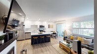 This thoughtfully designed single-floor residence showcases a seamless open-concept layout that connects the kitchen, dining, and living areas into one cohesive, light-filled space. The contemporary kitchen is equipped with stainless steel appliances — including a refrigerator, electric range, built-in microwave, and dishwasher — complemented by crisp white cabinetry, a decorative tile backsplash, quartz countertops, and a contrasting dark island with bar seating. The adjacent dining area flows naturally toward sliding glass doors that open to a private outdoor space, filling the interior with natural light. The living room features warm wood-look flooring, a fireplace with built-in shelving, and ample room for comfortable furnishings. The bedroom is carpeted and generously sized, boasting large windows with garden views, a walk-in closet, and a textured accent wall that adds warmth and character. A full bathroom with a tub-shower combination and wood-look flooring serves the space. A stacked in-unit washer and dryer provides added convenience. Recessed lighting throughout and a neutral color palette create a clean, modern ambiance across the entire residence.