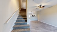 This two-story home is thoughtfully designed across two evenly sized floors, providing a functional and comfortable layout. The main level features an open-concept living room and kitchen area, where light-toned luxury vinyl plank flooring extends throughout. The living room is equipped with a ceiling fan and connects seamlessly to the kitchen, which boasts white shaker-style cabinetry, granite countertops, stainless steel appliances including a French door refrigerator and range, and a bright window overlooking the exterior. A convenient half or full bathroom is also located on this floor. Carpeted stairs with a wood railing lead to the upper level, where three bedrooms are situated. The primary bedroom offers a private en-suite bathroom featuring a white tub-shower surround with brushed nickel fixtures. The additional bedrooms are carpeted, each equipped with ceiling fans and windows that allow natural light. A hallway bathroom serves the secondary bedrooms. Neutral warm-beige walls, consistent trim work, and ceiling fans throughout both floors contribute to a cohesive and practical living environment.