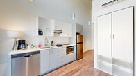 Located at 1611 NW Marshall St in Portland's vibrant Pearl District, this thoughtfully designed two-story unit makes exceptional use of its compact footprint across two levels. The ground floor is anchored by a sleek, modern kitchen outfitted with stainless steel appliances — including a full-size refrigerator, dishwasher, microwave, and cooktop — paired with crisp white upper cabinetry and light gray lower cabinets atop durable wood-look flooring. Soaring ceilings dramatically expand the sense of vertical space, while cylindrical pendant lighting adds a contemporary industrial touch. A built-in storage unit and a ladder staircase lead to the upper level, where a carpeted loft area offers a quiet, versatile space ideal for sleeping or a private retreat. A second kitchen on the upper floor mirrors the modern aesthetic of the first, providing added convenience and flexibility. Large floor-to-ceiling sliding glass doors open to a private balcony overlooking the surrounding neighborhood, filling the space with abundant natural light. A mini-split system ensures year-round climate comfort. The overall design is clean, minimalist, and efficiently planned — ideal for those seeking a smart urban living or investment opportunity in one of Portland's most walkable neighborhoods.