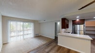 Located at 2460 Bear Valley in Escondido, unit #130 is a single-floor residence designed with a functional and comfortable layout. The open-concept living and dining area features a combination of wood-style hard flooring and plush carpeting, with a textured ceiling overhead. Large sliding glass doors with vertical blinds fill the space with natural light and provide access to an outdoor balcony area with views of the surrounding greenery. The kitchen is seamlessly integrated into the living space via a peninsula counter with light stone-style countertops, rich dark cabinetry, a stainless steel sink, and a full-size stainless steel refrigerator, offering ample storage and workspace. A dedicated entry area with wood-style flooring leads into the main living space. The bedrooms are carpeted and well-lit, each featuring vertical blinds and windows that invite natural light. The unit includes two bathrooms — one featuring a walk-in shower with a clean white surround and a dark wood vanity with mirror, and a second with a full bathtub and shower combination. Throughout, the neutral color palette and consistent finishes create a cohesive and practical living environment.