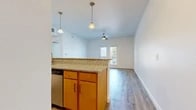 Located at 214 S Bell Ave in Denton, TX, this two-bedroom, one-bathroom unit offers a well-designed single-level layout. The open-concept kitchen and living area serves as the heart of the home, where a peninsula with granite countertops and pendant lighting separates the two spaces. The kitchen is equipped with warm wood cabinetry, stainless steel appliances including a refrigerator and microwave, and a built-in sink on the peninsula. The living room features durable hardwood-style flooring, a ceiling fan, and a set of French doors that open to a private balcony, inviting natural light and outdoor views. Both bedrooms are finished with plush carpeting, ceiling fans, and windows fitted with blinds for privacy. The primary bedroom includes a closet and connects to the hallway leading back to the main living area. The bathroom is appointed with warm wood vanity cabinetry, a white countertop, tiled tub-shower combo, and hardwood-style flooring. A dedicated laundry area and two hallways provide added functionality and convenience. The bright, neutral color palette throughout creates a clean and cohesive atmosphere across the entire unit.