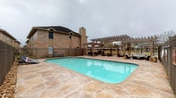 This single-story property offers a thoughtfully designed blend of indoor sophistication and outdoor leisure. The exterior showcases a generously sized swimming pool with an attached spa, surrounded by a stamped concrete deck that adds texture and visual warmth. A large wooden pergola extends over a portion of the patio, providing shaded seating and an ideal setting for outdoor gatherings. The area is enclosed by a wrought iron fence, offering both security and an open sightline to the surrounding landscape. The brick exterior of the building, complete with a chimney, adds a classic, grounded aesthetic to the property.

Inside, the dining area is a standout space defined by its refined, eclectic character. Dark hardwood-style flooring anchors the room, while crisp white walls and recessed lighting create a clean, gallery-like atmosphere. A striking round green marble dining table serves as the centerpiece, surrounded by woven rattan-style chairs atop a natural fiber rug. Large-scale abstract artwork adorns the wall, enhancing the artistic sensibility of the space. A rustic barn-style sliding door and a vintage glass-paneled door add distinctive architectural character, connecting the dining area to an adjacent hallway where additional framed artwork is displayed, reinforcing the space's curated, art-forward identity.