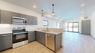 Located at 1247 Range St in Mankato, Minnesota, this well-designed two-bedroom, one-bathroom unit offers a thoughtful layout across a single floor. The open-concept kitchen and living area forms the heart of the space, bathed in natural light from large windows and sliding glass doors that lead to a private balcony. The kitchen is outfitted with sleek gray cabinetry, light countertops, and a full suite of stainless steel appliances including a refrigerator, electric range, over-the-range microwave, and dishwasher. Stylish pendant lighting accents the kitchen peninsula, while recessed lighting and light wood-style flooring add to the contemporary aesthetic throughout the main living area. Both bedrooms feature plush carpeting and windows that bring in natural light. The primary bedroom is generously sized and includes access to a walk-in closet outfitted with wire shelving for ample storage. The bathroom is clean and functional, featuring a walk-in shower with sliding glass doors, a gray vanity with brushed nickel hardware, and tile flooring. A dedicated utility room and additional closet space round out the unit's practical offerings, making this a well-appointed and efficient living space.