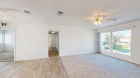 Located at 1025 S Beach St in Daytona Beach, Florida, this single-floor, three-bedroom, two-bathroom home offers a practical and comfortable layout. The combined living and dining area is bright and open, featuring a ceiling fan, neutral carpet, and wood-style flooring that transitions seamlessly between spaces. A large window and sliding glass door fill the area with natural light and provide access to an outdoor deck with views of the surrounding greenery and palm trees.

The kitchen is equipped with white cabinetry, a double-basin sink, a black electric range, and tile flooring. A window above the counter keeps the space well-lit, adding to the functional and clean aesthetic.

The three bedrooms are carpeted and well-sized, with the primary bedroom offering a notably generous footprint and a dedicated walk-in closet fitted with wire shelving. The additional bedrooms each include sliding or panel-door closets, and the home features a total of five closets for ample storage throughout.

The two bathrooms include a tiled tub-shower combination with classic fixtures. A dedicated laundry area and a central hallway connecting the rooms complete the layout. The home's clean, light-filled interior and practical design make it a functional residence in a convenient Daytona Beach location.