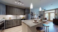 This single-story, one-bedroom, one-bathroom residence offers a thoughtfully designed open-concept layout that maximizes its well-proportioned footprint. Light wood-style flooring flows throughout the main living areas, creating a cohesive and contemporary aesthetic.

The kitchen serves as a central hub of the space, featuring dark wood-grain cabinetry, a classic white subway tile backsplash, under-cabinet lighting, and stainless steel appliances including a full-size refrigerator, range, microwave, and dishwasher. A granite-topped island with seating for two anchors the kitchen and provides additional prep and dining space, illuminated by modern pendant lighting. Track lighting adds further functionality overhead.

The living area is bright and welcoming, benefiting from large windows and French doors that invite natural light and outdoor views. A ceiling fan provides year-round comfort.

A dedicated laundry area is conveniently located off the kitchen, housing a full-size washer and dryer. The bathroom features large-format tile flooring, a granite vanity with wood-tone cabinetry, a soaking tub, and a separate shower. An adjacent walk-in closet with built-in shelving and hanging rods provides ample storage.