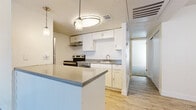 This single-floor space is thoughtfully laid out, offering a cohesive blend of functional design and clean, neutral finishes throughout. The kitchen serves as a central feature, equipped with stainless steel appliances including a refrigerator and electric range, white cabinetry providing ample storage, and grey stone-finish countertops. A peninsula with an overhang defines the kitchen boundary and creates an open pass-through to the main living area, enhanced by a trio of pendant lights overhead that add a modern touch. Light wood-tone vinyl plank flooring runs throughout the kitchen and living areas, lending warmth and continuity to the space.

The living area is generously proportioned and filled with natural light courtesy of a full-width sliding glass door fitted with vertical blinds, offering direct outdoor access. The textured ceiling adds subtle architectural character throughout the common areas.

The bedrooms feature soft wall-to-wall carpeting, creating a comfortable and quiet atmosphere. One bedroom includes a spacious walk-in closet outfitted with a double rod and shelf system, maximizing storage capacity. A window allows natural light to filter into the room. The overall palette of the space is light and neutral, with white walls and clean trim work contributing to an open, airy feel throughout.