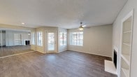 This single-story space combines comfort and modern design throughout its layout. The main living area is open and airy, featuring wood-look plank flooring that runs seamlessly throughout. Multiple windows fitted with white horizontal blinds allow generous natural light to fill the room, creating a bright and welcoming atmosphere. A ceiling fan centered in the living area provides both functionality and a finishing touch to the textured ceiling above. A glass-paneled exterior door adds additional light and offers a view to the outside. Neutral-toned walls complement the flooring and contribute to a clean, versatile aesthetic.

The kitchen is distinctly contemporary in style, showcasing dark espresso-toned cabinetry with sleek, linear hardware. Light-colored countertops provide a striking contrast against the darker elements, while a subway tile backsplash in soft, muted tones adds texture and visual interest. Black appliances, including a range and an over-the-range microwave, reinforce the modern character of the kitchen. The overall design of the space balances practicality with a cohesive, updated aesthetic suited to everyday living.