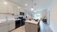 Located on High Lake Road in Winfield, Illinois, this single-floor residence offers a thoughtfully designed open-concept layout with modern finishes throughout. The kitchen serves as the centerpiece of the living space, featuring soft gray shaker-style cabinetry, white quartz countertops, a classic subway tile backsplash, and black appliances including a range, microwave, and dishwasher. A central island with pendant globe lighting provides additional prep space and casual seating, flowing seamlessly into the dining and living areas. Light-toned hardwood-style flooring runs throughout the main living spaces, enhancing the bright, airy atmosphere created by natural light from large windows and sliding glass doors. The living room offers a comfortable, open setting with ample wall space and access to the outdoors. The bedroom features plush carpeting and a generously sized window that allows for natural light, creating a calm and restful environment. Clean white walls and simple, modern door hardware are consistent design elements throughout. The bathroom is finished with the same light hardwood-style flooring, a glass-enclosed shower, white cabinetry, and a clean, minimalist aesthetic. Overall, the space presents a cohesive contemporary design with practical finishes ideal for comfortable everyday living.