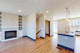 This contemporary multi-floor residence is designed with a clean, modern aesthetic throughout its three levels. The main living area centers around an open-concept layout where the kitchen flows seamlessly into the living room. The kitchen is outfitted with white shaker cabinetry, granite countertops, stainless steel appliances including a French door refrigerator and range, a patterned tile backsplash, and a central island with pendant globe lighting overhead. The living room features light hardwood-style flooring, a built-in fireplace flanked by open shelving, and a sliding glass door that invites natural light and outdoor access.

Bedrooms are carpeted and generously windowed, offering views of the surrounding neighborhood and filling the rooms with natural light. A ceiling fan provides additional comfort. The bathrooms are well-appointed, featuring granite-topped white vanities, large mirrors, brushed gold fixtures, and subway tile surrounds in the tub-shower combinations. Hardwood-style flooring carries through the bathroom spaces for a cohesive look.

Additional highlights include a dedicated in-unit laundry area with a full-size washer and dryer, a walk-in closet with wire shelving, and recessed lighting throughout. The overall ambiance is bright, clean, and move-in ready.