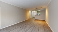 The Exeter floorplan at 55 Cedar St in Woburn, MA presents a thoughtfully designed two-bedroom, one-bathroom residence on a single level. The open-concept living room and kitchen area form the heart of the home, featuring light wood-style flooring, crown molding, and track lighting that enhances the bright, airy atmosphere. The kitchen is well-appointed with white shaker-style cabinetry, granite-look countertops, a stainless steel refrigerator, range, and over-the-range microwave, along with a peninsula that connects seamlessly to the living area. Both bedrooms are comfortably sized, with the spacious primary bedroom offering generous proportions and plush wall-to-wall carpeting. Natural light fills the bedrooms through well-positioned windows that frame outdoor views. The second bedroom also features soft carpeting and a bright window. The full bathroom is finished with wood-style flooring, a white vanity with a countertop sink, and clean, neutral tones throughout. Consistent warm-gray wall tones and white trim unify the space, creating a cohesive and modern aesthetic. The efficient single-floor layout ensures easy accessibility and functional flow between all rooms, making this residence a practical and attractive home.