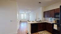 This single-floor residence offers a thoughtfully designed open-concept layout that seamlessly connects the kitchen and living area. The kitchen is a functional centerpiece, featuring rich dark-wood cabinetry, light countertops, a full suite of black appliances including a range, over-the-range microwave, refrigerator, and dishwasher, as well as a peninsula with a double sink that opens directly to the main living space. Track lighting and a ceiling fan keep the area well-lit and comfortable. Warm hardwood-style flooring flows consistently throughout the entire residence, lending a cohesive and inviting feel to every room. The living area is bright and open, benefiting from natural light through multiple windows. The bedrooms are generously sized, each equipped with a ceiling fan and windows that allow for ample natural light. The bathrooms mirror the design language of the rest of the home, featuring rich wood-toned vanity cabinetry, white countertops, large mirrors, and hardwood-style flooring. One bathroom includes a shower/tub combination. The overall palette of crisp white walls paired with warm wood tones creates a clean, modern, and welcoming atmosphere throughout the space.
