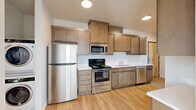 This single-floor unit offers three bedrooms, one bathroom, a kitchen, a living room, and a closet, making efficient use of its compact footprint. Light wood-tone flooring runs consistently throughout, creating a cohesive and clean aesthetic across all rooms.

The kitchen is well-appointed with a full suite of stainless steel appliances, including a refrigerator, electric range, microwave, and dishwasher. Warm-toned wood cabinetry extends to the ceiling, providing generous storage, while light countertops and a single-basin sink complete the functional layout.

The bedrooms feature neutral walls, natural light from windows with blinds, and light hardwood-style flooring. The primary bedroom is the largest of the three, offering a comfortable footprint. One bedroom includes a closet with bifold doors, and another features multiple windows that allow ample sunlight.

The bathroom is finished in a clean, white palette with a tub-shower combination, wood-style flooring, a toilet, and a window for natural ventilation. The hallway connects the rooms efficiently, with recessed lighting overhead and white panel doors throughout, contributing to the unit's bright, modern character.