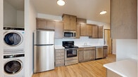 This single-floor unit offers three bedrooms, one bathroom, a kitchen, a living room, and a closet, making efficient use of its compact footprint. Light wood-tone flooring runs consistently throughout, creating a cohesive and clean aesthetic across all rooms.

The kitchen is well-appointed with a full suite of stainless steel appliances, including a refrigerator, electric range, microwave, and dishwasher. Warm-toned wood cabinetry extends to the ceiling, providing generous storage, while light countertops and a single-basin sink complete the functional layout.

The bedrooms feature neutral walls, natural light from windows with blinds, and light hardwood-style flooring. The primary bedroom is the largest of the three, offering a comfortable footprint. One bedroom includes a closet with bifold doors, and another features multiple windows that allow ample sunlight.

The bathroom is finished in a clean, white palette with a tub-shower combination, wood-style flooring, a toilet, and a window for natural ventilation. The hallway connects the rooms efficiently, with recessed lighting overhead and white panel doors throughout, contributing to the unit's bright, modern character.