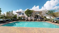 This single-floor residence is part of a well-appointed Mediterranean-inspired community, distinguished by its stucco exterior, decorative architectural detailing, and a warm, resort-like atmosphere. The standout feature of the property is the expansive outdoor pool area, where clear turquoise water is framed by a classic brick-paver deck. A generous arrangement of sling-style lounge chairs lines the poolside, offering ample space for relaxation and recreation. Mature palm trees and ornamental plantings provide natural shade and privacy, while a wrought-iron perimeter fence adds both definition and security to the outdoor space. The multi-story building backdrop showcases arched accents, symmetrical window arrangements, and a tiled roofline characteristic of Florida Mediterranean architecture. The open-sky setting allows abundant natural light to fill the outdoor areas, creating a bright and inviting ambiance throughout the day. The overall environment reflects a carefully maintained, community-oriented setting with a strong emphasis on outdoor living and leisure, making the pool deck a central gathering point for residents enjoying the warm climate and scenic surroundings.