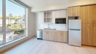 This 240 square foot studio apartment in Seattle showcases efficient urban living. The space features a modern, well-equipped kitchen with light wood cabinetry, white countertops, and stainless steel appliances including a dishwasher and refrigerator. A subway tile backsplash and open shelving add style and functionality.

The bathroom is compact yet functional, with a toilet, vanity, and shower stall. In-unit laundry facilities, including a stacked washer and dryer, are conveniently integrated into the space.

Light-colored walls and floors create an airy atmosphere, while a large window allows natural light to flood the main living area. The neutral color palette and minimalist design contribute to a sense of spaciousness in the compact layout.

Despite its small footprint, the apartment efficiently accommodates all essential living functions, making it an ideal choice for those seeking a low-maintenance urban lifestyle in the heart of Seattle.