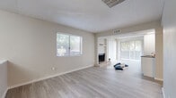 This single-floor unit offers a clean, modern aesthetic throughout, highlighted by light wood-look flooring and neutral warm-toned walls that create a welcoming, cohesive atmosphere. The expansive open-plan living and dining area is a standout feature, bathed in natural light from multiple windows dressed with horizontal blinds and a large sliding glass door with vertical blinds that opens to an outdoor area. A classic brick fireplace with a built-in shelf above serves as the focal point of the living space, adding a timeless character to the otherwise contemporary interior. A textured popcorn ceiling adds a distinctive finish throughout the main living areas. The galley-style kitchen is thoughtfully designed with white shaker cabinetry, dark granite countertops, a white subway tile backsplash, and stainless steel appliances including a dishwasher and refrigerator, providing ample storage and workspace. The bathroom mirrors the kitchen's refined style, featuring white shaker vanity cabinets topped with a dark granite countertop, a single undermount sink, and a framed mirror. Light wood-look flooring continues seamlessly into the bathroom, reinforcing the space's unified design. Overall, this unit presents a well-maintained, move-in ready interior with a bright and airy ambiance.