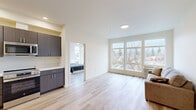 Located at 3910 N Wall St in Spokane, WA, this thoughtfully designed 2-bedroom, 2-bathroom unit offers a clean, modern aesthetic throughout. Light wood-style flooring flows consistently across all rooms, creating a bright and cohesive feel. The open living area is anchored by a large multi-pane window that frames pleasant outdoor views of the surrounding neighborhood, filling the space with natural light. Adjacent to the living room, the kitchen is outfitted with dark wood-grain cabinetry, white quartz countertops, a black matte sink, and stainless steel appliances including a range and over-the-range microwave. The primary bedroom is a standout feature, boasting corner windows on two walls that flood the room with light and offer expansive views, complemented by a ceiling fan. The second bedroom also benefits from natural light through its own window. Both bathrooms are finished with dark wood vanities, white countertops, round framed mirrors, and modern matte black hardware, continuing the contemporary design language. A dedicated closet with built-in wire shelving provides practical storage. The unit also includes a dedicated entrance, rounding out a well-organized and functional floor plan.