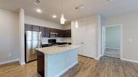 This single-floor 2-bedroom, 2-bathroom residence combines modern design with functional living. The heart of the home is an open-concept kitchen featuring a large center island with a granite countertop and undermount sink, illuminated by sleek pendant lighting. Dark espresso cabinetry provides ample storage and contrasts beautifully with the light granite surfaces, while stainless steel appliances — including a refrigerator, range, and microwave — complete the contemporary look. A tile backsplash adds a refined touch, and wood-look flooring runs throughout the main living and kitchen areas, adding warmth and continuity.

The two bedrooms are carpeted for comfort and offer generous proportions, with neutral tones creating a calm and restful ambiance. One bedroom features a window with blinds, allowing for natural light. The primary bathroom is well-appointed with a dark vanity, granite countertop, a large framed mirror, a lighted vanity bar, and a walk-in shower, all set on wood-look flooring. The second bathroom includes a full tub-shower combination with clean white tile surround. A double-door storage closet near the kitchen provides additional organizational space, rounding out this thoughtfully designed residence.