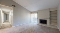 This single-floor, 2-bedroom, 2-bathroom residence offers a thoughtfully designed layout that maximizes comfort and functionality. The living room serves as the heart of the home, featuring soaring vaulted ceilings that create an airy, open feel, soft wall-to-wall carpeting, and a classic white brick fireplace flanked by built-in shelving. A sliding glass door floods the space with natural light and provides access to the outdoors. The kitchen is well-appointed with white shaker cabinetry, stainless steel appliances including a range and dishwasher, a mosaic tile backsplash, light countertops, and wood-look flooring — a clean and functional workspace for everyday cooking. Both bedrooms are carpeted and offer ample natural light through large windows, with each room serviced by a dedicated closet featuring bifold doors and full-length hanging rods. The two bathrooms are finished with wood-look tile flooring, white vanities, and full tub-shower combinations with white tile surrounds and brushed gold hardware. A dedicated laundry area adds everyday convenience, while a hallway connects the space cohesively. Together, these features make for a comfortable and practical living environment.