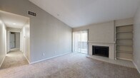 This single-floor, 2-bedroom, 2-bathroom residence offers a thoughtfully designed layout that maximizes comfort and functionality. The living room serves as the heart of the home, featuring soaring vaulted ceilings that create an airy, open feel, soft wall-to-wall carpeting, and a classic white brick fireplace flanked by built-in shelving. A sliding glass door floods the space with natural light and provides access to the outdoors. The kitchen is well-appointed with white shaker cabinetry, stainless steel appliances including a range and dishwasher, a mosaic tile backsplash, light countertops, and wood-look flooring — a clean and functional workspace for everyday cooking. Both bedrooms are carpeted and offer ample natural light through large windows, with each room serviced by a dedicated closet featuring bifold doors and full-length hanging rods. The two bathrooms are finished with wood-look tile flooring, white vanities, and full tub-shower combinations with white tile surrounds and brushed gold hardware. A dedicated laundry area adds everyday convenience, while a hallway connects the space cohesively. Together, these features make for a comfortable and practical living environment.