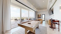 Located at 10401 Washington Blvd in Culver City, Los Angeles, this rooftop amenity space delivers a seamless blend of indoor comfort and outdoor living. The interior lounge features high ceilings with recessed lighting, light tile flooring in a herringbone pattern, and a full-size billiard table as a central focal point. A built-in bar with bar seating and a wall-mounted flat-screen TV anchors one side of the room, while oversized sliding glass walls span the full width of the space, dissolving the boundary between indoors and out. The transition to the outdoors is marked by warm wood deck tiles that carry across the covered terrace, where café-style bistro tables provide casual seating. Steps lead down to the expansive open-air rooftop terrace, where a sparkling lap pool is surrounded by turf lawn, lounge chairs, and dedicated sunbathing areas. An outdoor kitchen and pergola-shaded lounge complete the rooftop experience. Sweeping panoramic views of the Los Angeles skyline and surrounding Culver City neighborhood stretch across the horizon, making this a remarkable amenity space designed for both relaxation and social gatherings.