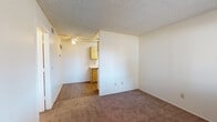Located at 6161 E Grant Rd in Tucson, Arizona, this single-floor unit offers a straightforward and functional layout designed for comfortable everyday living. The living area features warm, neutral-toned carpet underfoot, white walls, and a textured ceiling, creating a clean and understated atmosphere. A ceiling fan provides airflow, while a front-facing window fitted with horizontal blinds allows natural light to fill the space and offers a view of the surrounding area. The entry door opens directly into the living area, transitioning from hardwood-style flooring at the threshold to carpet throughout the main space. The galley-style kitchen is efficiently arranged with wood-toned cabinetry lining both sides, providing ample storage. It includes a double coil electric range, a full-size refrigerator, a single-basin sink with adjacent counter space, and hardwood-style flooring that runs the length of the kitchen. The bedroom is a well-proportioned, carpeted room with a window that brings in natural light and a door providing privacy. The bathroom is clean and functional, featuring a full soaking tub with a shower, a single vanity with a laminate countertop, a medicine cabinet mirror, and hardwood-style flooring, giving it a bright and practical finish.