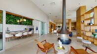 Located at 900 Pacific St in Stamford, Connecticut, this sophisticated amenity floor offers a rich array of curated spaces designed for relaxation, wellness, and socializing. The expansive main lounge is defined by soaring ceilings, large-format tile flooring, and dramatic floor-to-ceiling windows that flood the interior with natural light and frame views of the surrounding outdoor terrace. A striking suspended fireplace serves as the centerpiece of the lounge, complemented by mid-century modern furnishings, warm wood accents, and elegant pendant lighting. An adjoining dining and kitchen area features a vibrant green living wall, adding a natural, organic touch to the contemporary design. A game and reading nook offers a round table beneath a sculptural chandelier, flanked by a built-in wood shelving display. The spa area is a standout destination, highlighted by a serene indoor water feature with a lush planted surround, a glass-enclosed sauna with teak wood finishes, a dedicated relaxation lounge, and a full-service salon with glass-partitioned interiors. A gold-railed staircase connects the levels while overlooking the tranquil water installation. Throughout, the design balances refined materials with an open, welcoming ambiance.