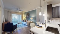 This single-story residence offers a thoughtfully designed open-concept layout connecting the living, dining, and kitchen areas. The living room serves as the centerpiece, featuring crown molding, wood-look flooring, a ceiling fan, and a striking teal accent wall. A large sliding glass door floods the space with natural light and provides outdoor access. The kitchen is outfitted with dark espresso cabinetry, stainless steel appliances including a range and built-in microwave, white quartz countertops, a tile backsplash, and a breakfast bar with pendant lighting overhead. The adjacent dining area accommodates a full-sized table and features track lighting and crown molding. The bedroom includes plush carpeting, a ceiling fan, a large window with outdoor views, and a walk-in closet with built-in shelving. The bathroom offers a dark-framed vanity with quartz countertop, large-format tile surround, and a soaking tub-shower combination. A dedicated in-unit laundry area with side-by-side washer and dryer and overhead shelving completes the layout.