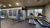 Located at 3601 S Lake Mary Rd in Flagstaff, Arizona, this fitness center offers a well-equipped, single-floor exercise space designed to accommodate a range of workout routines. The room features durable rubber flooring throughout, providing both safety and comfort during exercise sessions.

The space is outfitted with a comprehensive selection of equipment, including multiple treadmills, an elliptical trainer, a stationary bike, and a cable cross machine with an adjustable bench — suitable for both strength training and cardiovascular workouts. A full dumbbell rack lines one wall, complemented by medicine balls and additional free weight accessories. Large wall-mounted mirrors enhance the sense of space while allowing users to monitor their form.

Natural light flows in through multiple windows positioned along the walls, offering pleasant views of the surrounding wooded Flagstaff landscape — a refreshing backdrop during workouts. Recessed ceiling lighting ensures the space remains well-lit at all hours. A wall-mounted flat-screen television adds an entertainment option for users during cardio sessions.

The interior walls are finished in a combination of soft green-gray and neutral tones, contributing to a calm, focused atmosphere. Posted gym rules and a safety alarm system reflect an attention to user safety and facility management. Overall, this fitness center provides a functional, well-maintained environment suited for a variety of fitness goals.