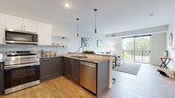 This well-designed single-floor residence showcases a thoughtful open-concept layout that seamlessly connects the kitchen, dining, and living areas. The kitchen is a standout feature, equipped with stainless steel appliances including a range, built-in microwave, and dishwasher. Two-tone cabinetry—white upper cabinets paired with dark lower cabinets—frames a gray subway tile backsplash, while pendant lighting and a peninsula with bar seating add both style and functionality. Warm hardwood-style flooring runs throughout the main living areas, complementing the light, neutral color palette.

The living area is bright and inviting, benefiting from natural light and direct access to a private balcony through a sliding glass door, offering pleasant outdoor views. Two well-proportioned bedrooms feature plush carpeting, large windows, and ample closet space.

The bathroom is appointed with a bold navy-blue vanity, gray countertop, and a large mirror with overhead lighting. A dedicated laundry area with a stacked washer and dryer and built-in shelving adds notable everyday convenience. Overall, the space presents a clean, contemporary aesthetic with practical, high-quality finishes throughout.
