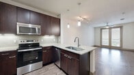 Located at 5811 Worth Pkwy in San Antonio, TX, this one-bedroom unit offers a thoughtfully designed single-level layout that maximizes functionality within a compact footprint. The open-concept kitchen and living area serves as the heart of the space, featuring rich dark-espresso cabinetry extending to the ceiling for ample storage, stainless steel appliances including a full-size refrigerator, electric range, and microwave, and a granite-topped peninsula with pendant lighting overhead. Tile backsplash and under-cabinet lighting add a polished finish to the kitchen. Wood-style flooring runs throughout the main living area, complemented by a ceiling fan and French doors that invite natural light and provide outdoor access.

The generously sized bedroom is finished with plush carpet, a ceiling fan, and a large window framing outdoor views. It connects to a dedicated walk-in closet outfitted with dual hanging rods and built-in shelving on multiple walls, offering well-organized storage capacity. Neutral wall tones and consistent trim work throughout create a cohesive, clean aesthetic. Ceiling fans in both the living area and bedroom contribute to year-round comfort across this efficiently designed San Antonio residence.